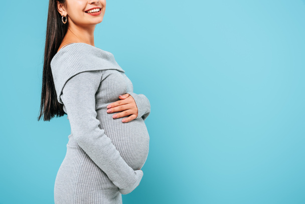 side view of smiling pregnant pretty girl touching belly isolated on blue - Foto, Imagem