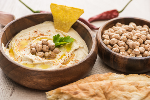 close up view of delicious hummus with chickpeas in bowl near fresh baked pita on beige wooden table - Foto, Bild