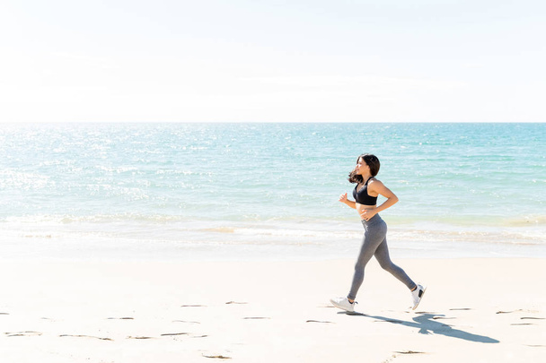 Widok z boku młoda kobieta jogging na brzegu morza na plaży podczas wakacji letnich - Zdjęcie, obraz