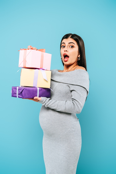 shocked pregnant pretty girl holding presents isolated on blue - 写真・画像