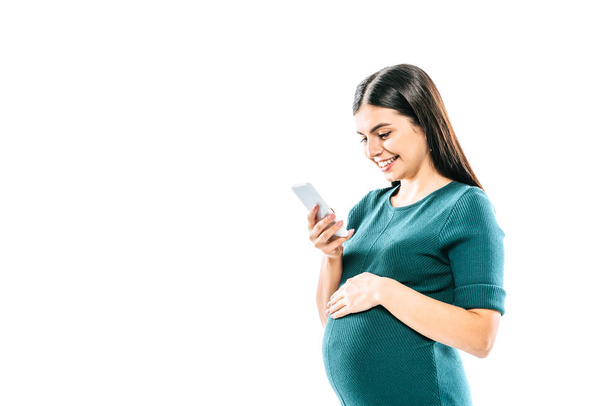smiling pregnant girl using smartphone isolated on white - Fotó, kép