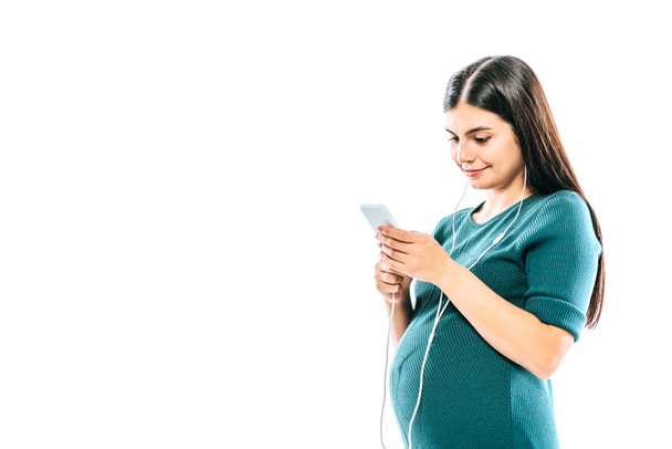 улыбающаяся беременная девушка с помощью смартфона и прослушивания музыки в наушниках изолированы на белом
 - Фото, изображение