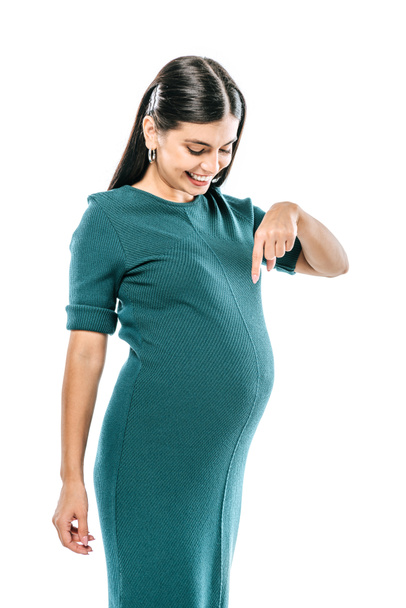 smiling pregnant girl pointing with finger at belly isolated on white - Foto, afbeelding