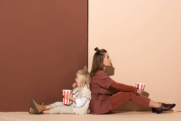 back to back view of daughter eating popcorn and attractive mother on beige and brown background  - Foto, immagini
