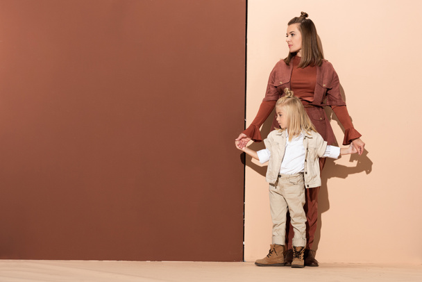 cute daughter and attractive mother holding hands on beige and brown background  - Φωτογραφία, εικόνα