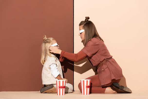 side view of mother wearing 3d glasses on daughter on beige and brown background  - Photo, Image