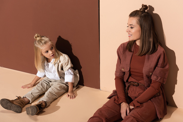 daughter talking with smiling mother and sitting on beige and brown background  - Valokuva, kuva