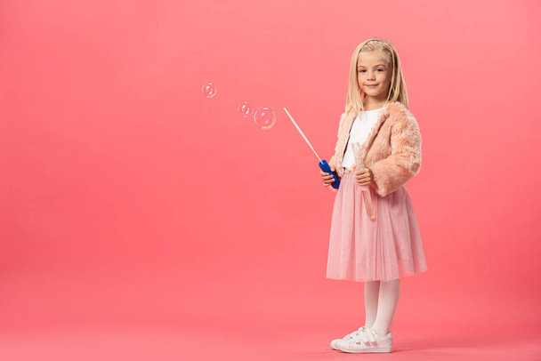 мила і усміхнена дитина тримає пляшку з мильними бульбашками на рожевому фоні
  - Фото, зображення
