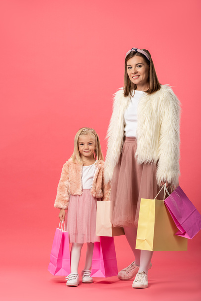 χαμογελαστή κόρη και μητέρα κρατώντας τσάντες για ψώνια σε ροζ φόντο  - Φωτογραφία, εικόνα