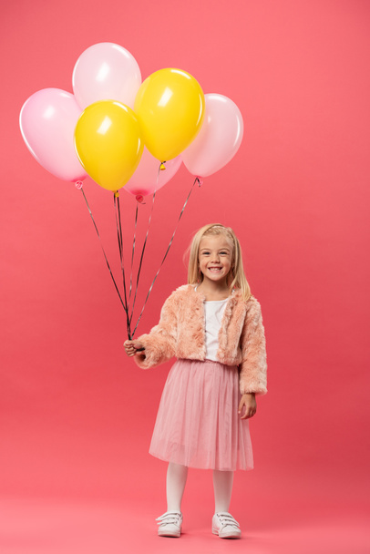 cute and smiling kid holding balloons on pink background  - Foto, Bild