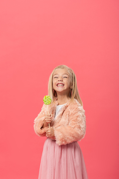 χαμογελαστό και χαριτωμένο παιδί κρατώντας γλειφιτζούρι απομονωμένο σε ροζ - Φωτογραφία, εικόνα