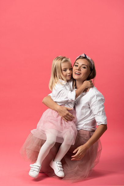 cute daughter hugging smiling mother on pink background  - Zdjęcie, obraz