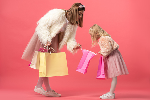 Schockierte Tochter und Mutter blicken auf Einkaufstasche auf rosa Hintergrund  - Foto, Bild