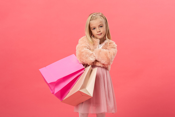 cute kid with crosses arms holding shopping bags isolated on pink - 写真・画像