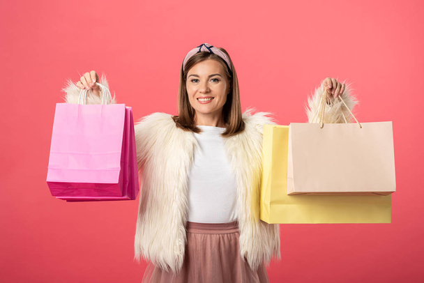 attractive and smiling woman holding shopping bags isolated on pink - Photo, Image