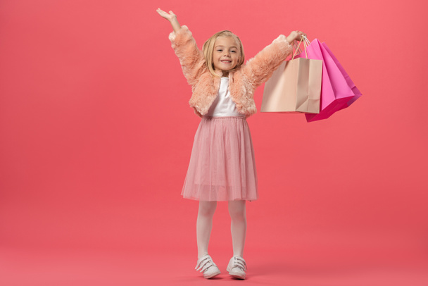 garoto bonito e sorridente com as mãos estendidas segurando sacos de compras no fundo rosa
  - Foto, Imagem