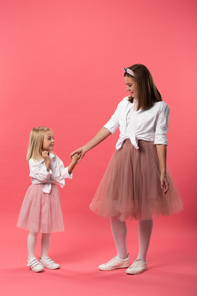 smiling daughter and mother holding hands on pink background  - Fotó, kép