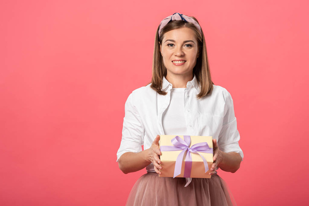 attractive and smiling woman holding gift box isolated on pink - Fotó, kép