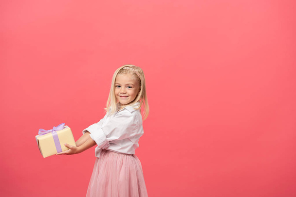 cute and smiling kid holding gift isolated on pink - Photo, Image