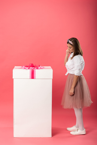 attractive and pensive woman standing near gift box on pink background  - Φωτογραφία, εικόνα