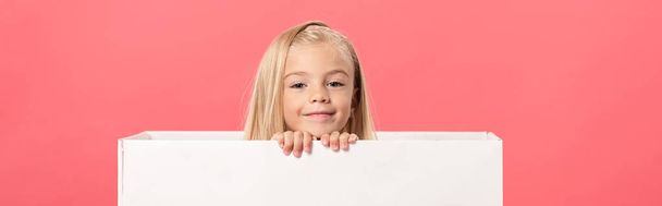 panoramic shot of cute and smiling kid in gift box isolated on pink - Foto, immagini