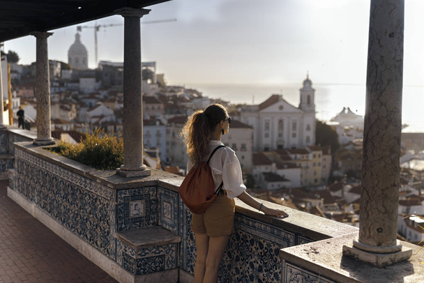 Ένας νεαρός τουρίστας στέκεται στο μπαλκόνι και κοιτάζοντας μια θέα στην ακτή της ευρωπαϊκής πόλης - Φωτογραφία, εικόνα