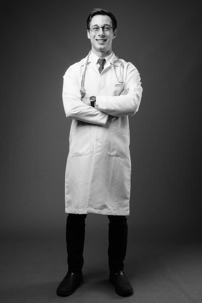 Young handsome man doctor against gray background in black and white - Fotó, kép