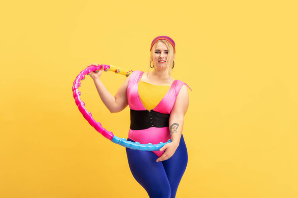 Young caucasian plus size female models training on yellow background - Foto, afbeelding