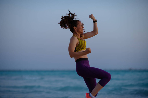 fit woman in fitness clothes on the ocean shore in the evening doing HIIT workout. - Foto, Imagen