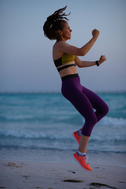 Full length portrait of young sports woman in sport clothes on the beach in the evening workout. - Фото, изображение