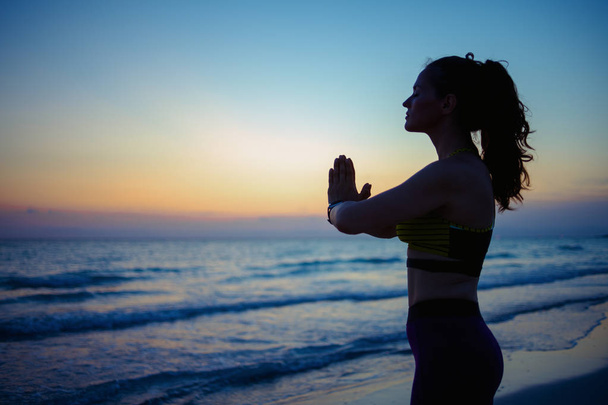 Silhouette of young woman in fitness clothes on the seacoast in the evening doing yoga. - Fotoğraf, Görsel