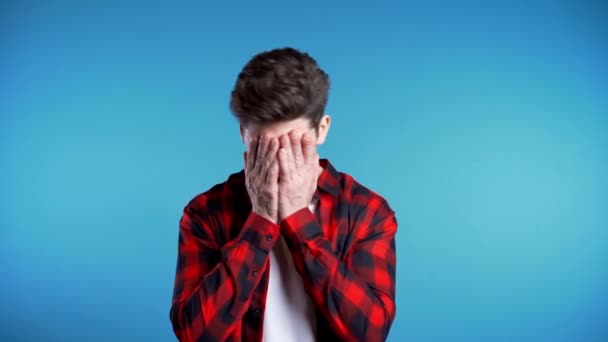 Young guy covers his face with hands from fatal disappointment, failure. Depressed lost man in red plaid shirt. Drama, emotions concept. 4k - Video