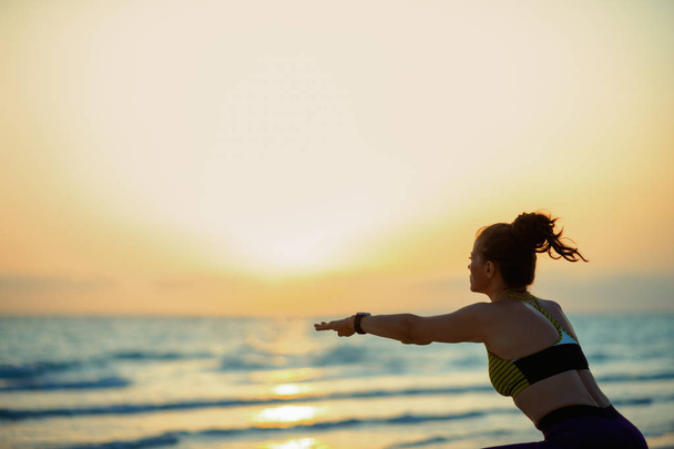 Silhouette of fit sports woman in sport clothes on the beach in the evening doing squats. - Φωτογραφία, εικόνα