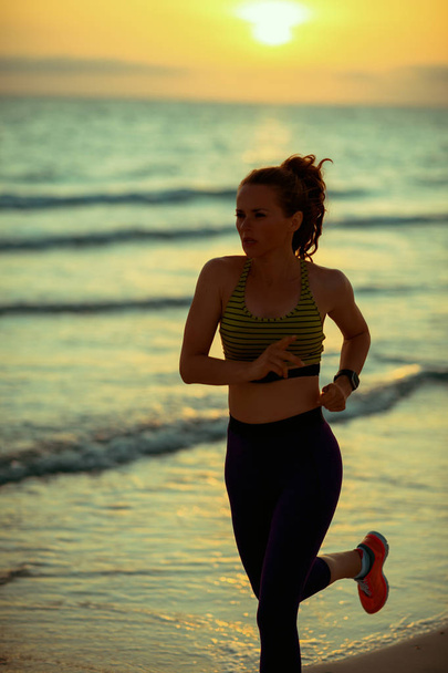 Silhouette of fit woman in sport clothes on the ocean shore at sunset jogging. - Fotoğraf, Görsel