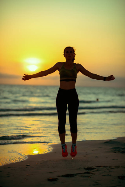 Silhouette of active sports woman in sport clothes on the beach at sunset doing HIIT workout. - Foto, Imagem