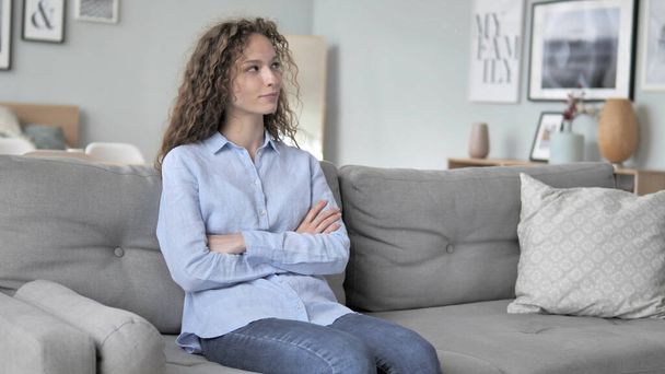 Frau mit lockigem Haar sitzt zu Hause auf Couch - Foto, Bild
