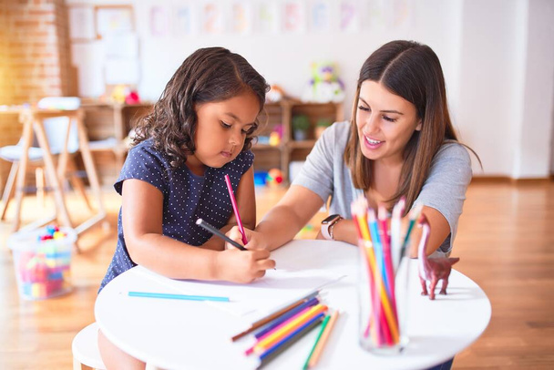 Hermosa maestra y niña dibujando dibujo utilizando lápices de colores en el jardín de infantes
 - Foto, Imagen