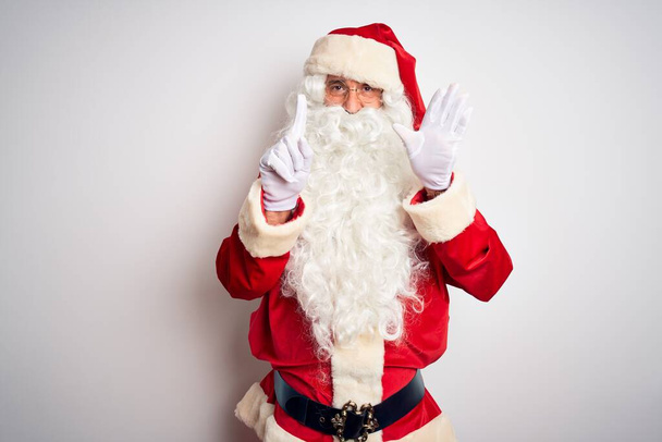 Hombre guapo de mediana edad vistiendo traje de Santa de pie sobre fondo blanco aislado mostrando y apuntando hacia arriba con los dedos número seis mientras sonríe confiado y feliz
. - Foto, Imagen