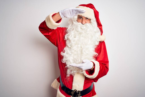 Ein gutaussehender Mann mittleren Alters im Weihnachtsmannkostüm steht vor isoliertem weißen Hintergrund und gestikuliert mit Händen, die ein großes und großes Zeichen, ein Maßsymbol, zeigen. Lächelnd in die Kamera blickend. Messkonzept. - Foto, Bild