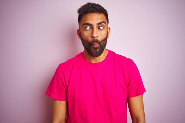 Young indian man wearing t-shirt standing over isolated pink background making fish face with lips, crazy and comical gesture. Funny expression. - Fotografie, Obrázek