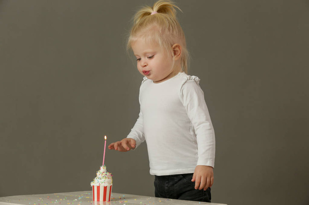 Студійний знімок дівчинки-малятка, що дме свічку на день народження з кексу
 - Фото, зображення