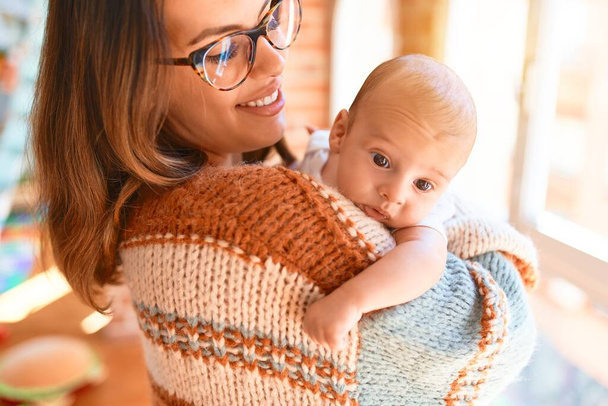 Young beautiful woman and her baby standing at home. Mother holding and hugging newborn - Foto, Imagem