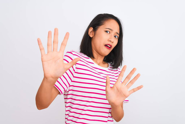Jeune femme chinoise portant t-shirt rayé debout sur fond blanc isolé peur et terrifié par l'expression de la peur arrêter geste avec les mains, criant en état de choc. Concept de panique
. - Photo, image