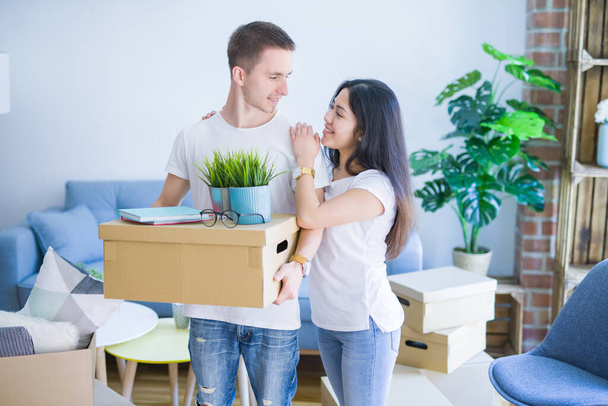 Young beautiful couple sitting on the sofa drinking coffee at new home around cardboard boxes - Photo, Image