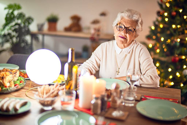 Adorable senior woman smiling happy and confident. Sitting prepared to celebrate christmas at home - Photo, Image