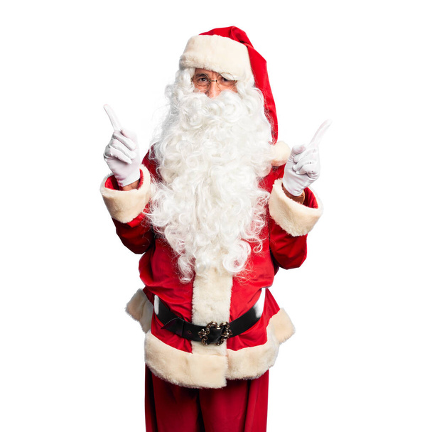 Красивый мужчина средних лет в костюме Санта-Клауса и с бородой, уверенно улыбающийся, указывая пальцами в разные стороны. Копирование места для рекламы
 - Фото, изображение