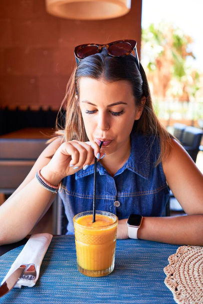 Nuori kaunis nainen istuu ravintolassa nauttien kesälomasta juoden terveellistä smoothie
 - Valokuva, kuva