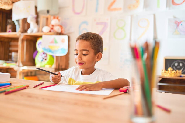 Krásné africké americké batole sedí kresba pomocí papíru a tužky na stole ve školce - Fotografie, Obrázek