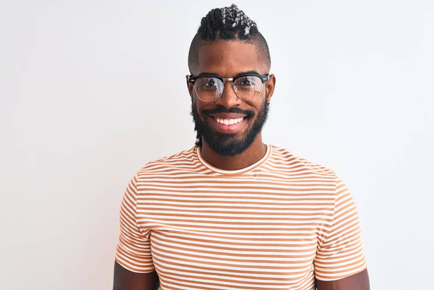 Afro-Amerikaanse man draagt gestreept t-shirt en bril over geïsoleerde witte achtergrond met een vrolijke en coole glimlach op het gezicht. Geluksvogel. - Foto, afbeelding