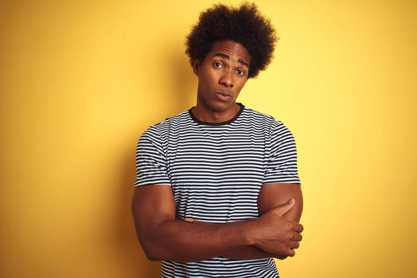 Afrikai amerikai férfi afro hajjal, tengerész csíkos pólót visel izolált sárga háttér szkeptikus és ideges, rosszalló arckifejezéssel, keresztbe tett karokkal. Negatív személy. - Fotó, kép